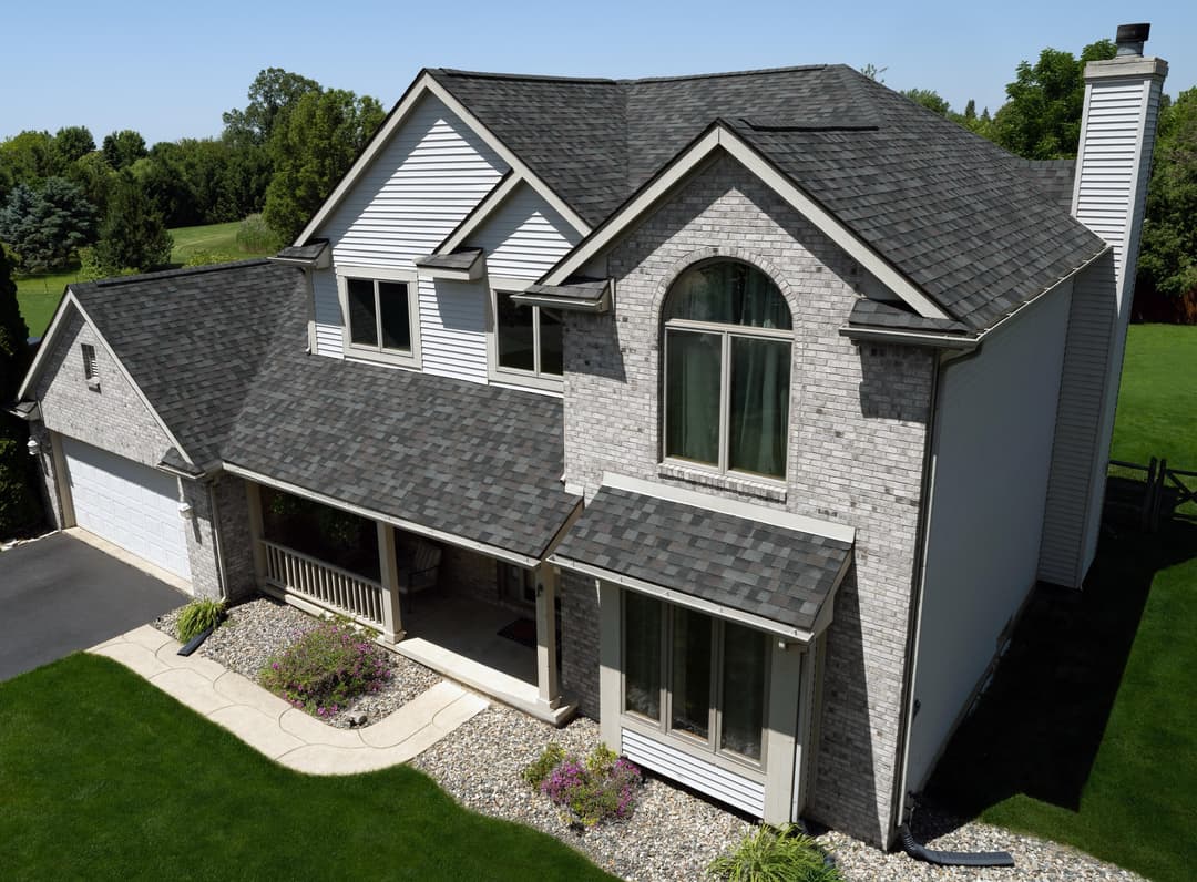 Aerial view of a modern house with gray shingles, stone facade, and landscaped yard.