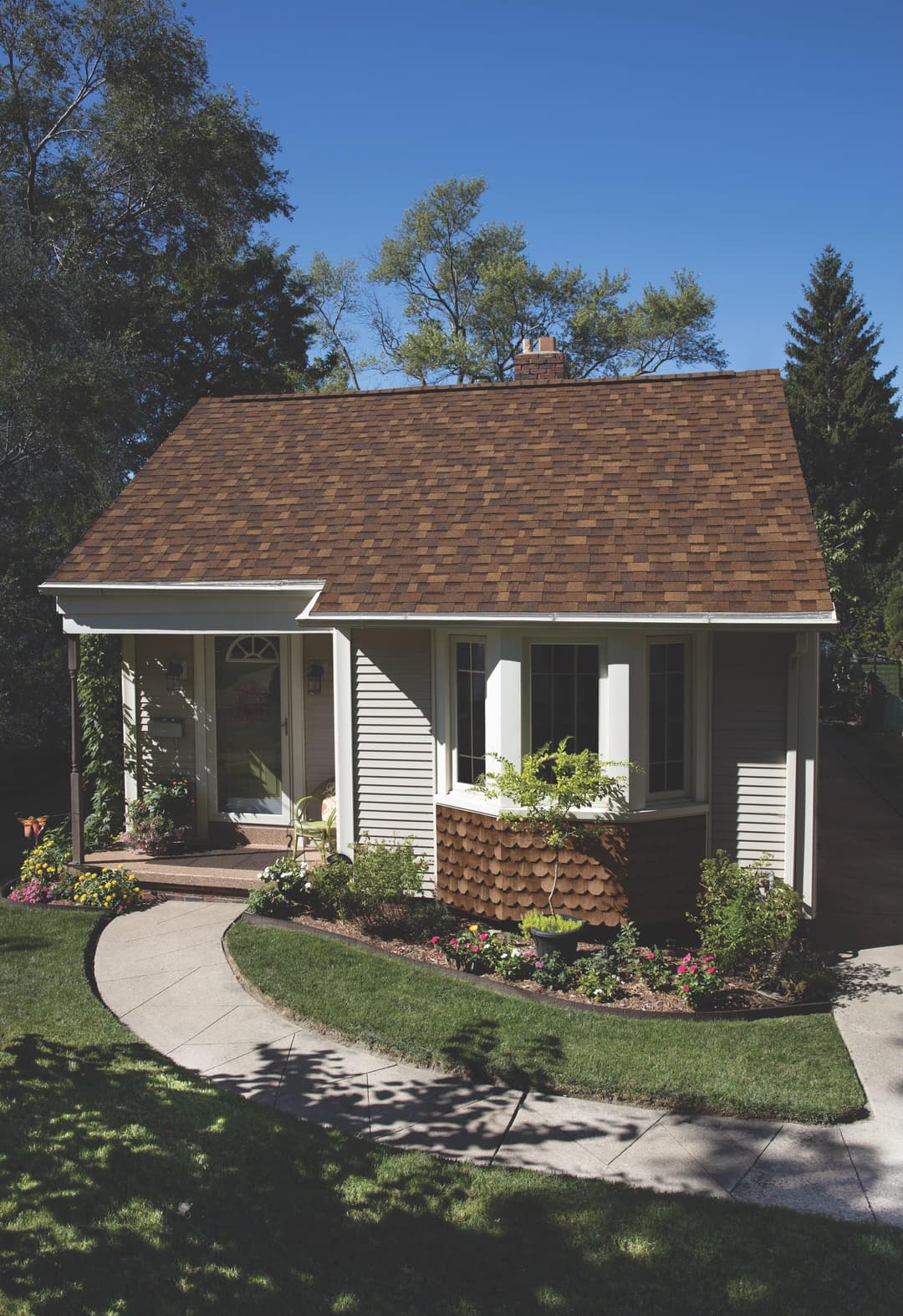 Charming small house with a brown shingle roof and landscaped garden under clear blue sky.
