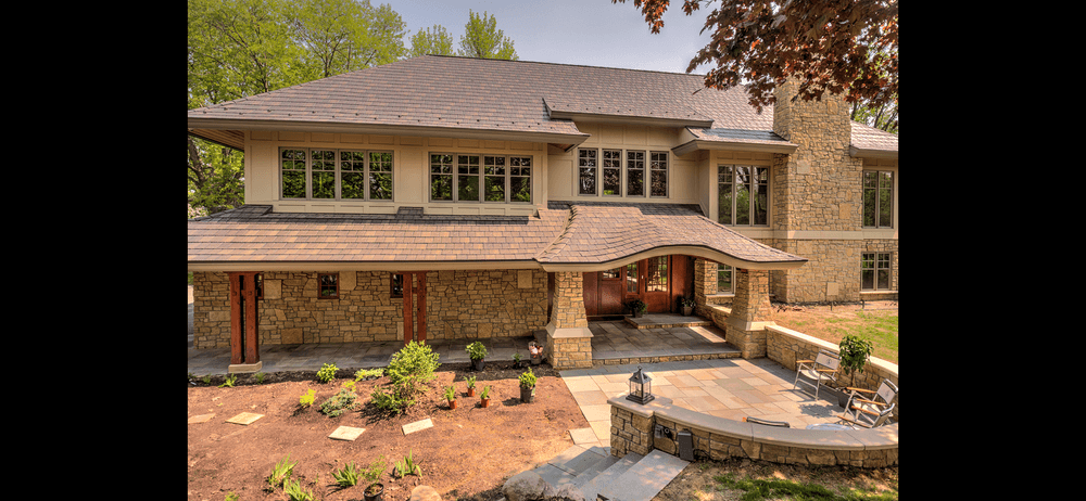 Modern stone house with large windows, landscaped garden, and patio seating area.