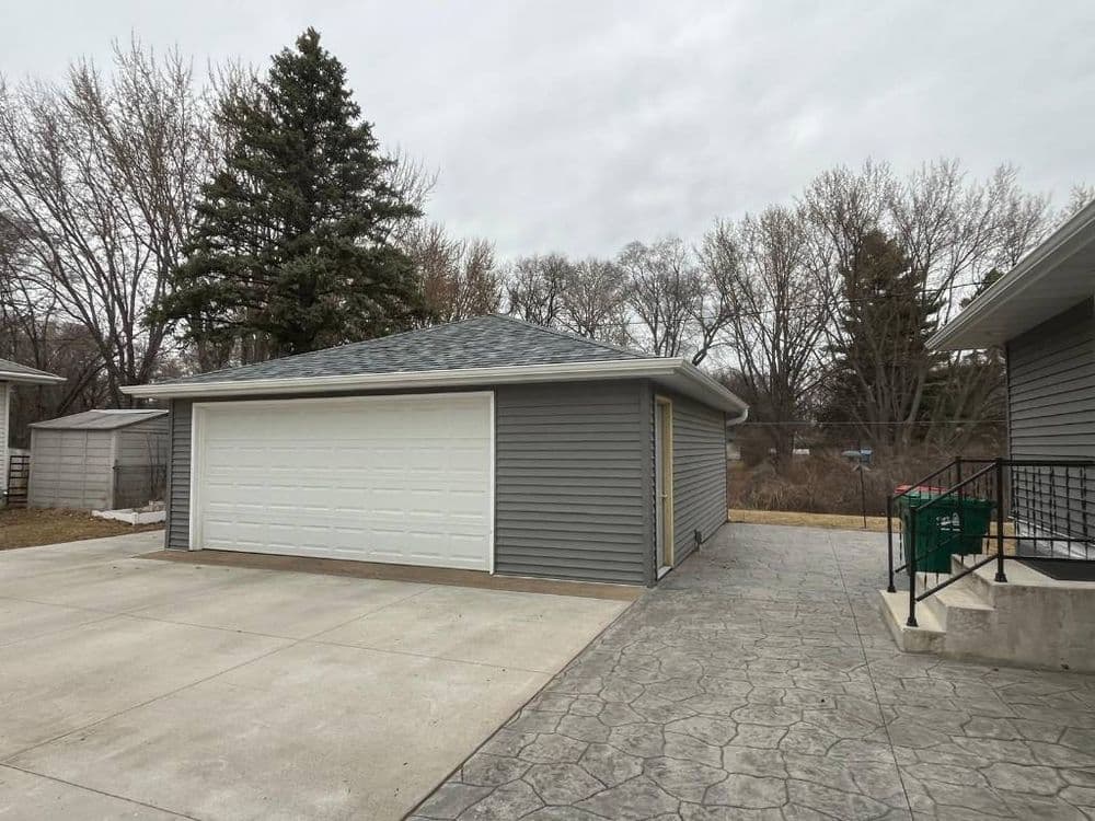 Gray garage with a white door, surrounded by trees and a concrete driveway.