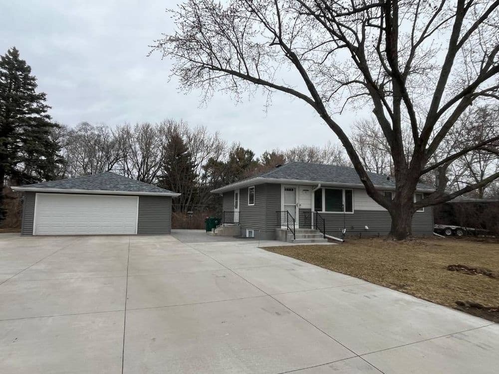 Single-story gray house with a garage, large driveway, and bare trees in a suburban setting.