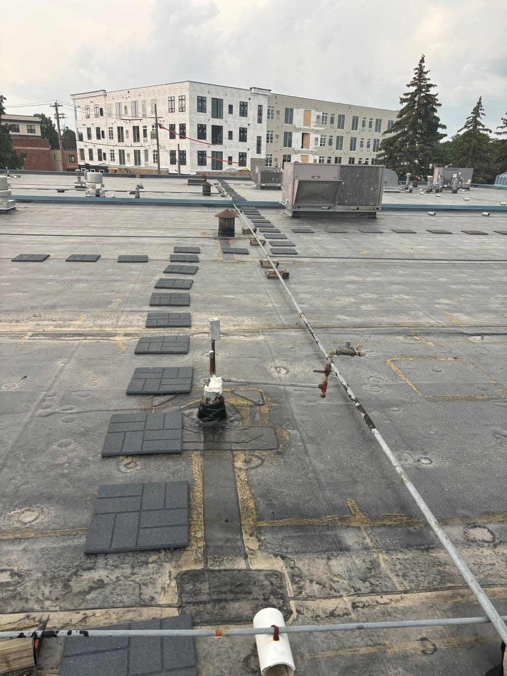 Flat commercial roof with gray shingles, HVAC units, and nearby modern building in background.