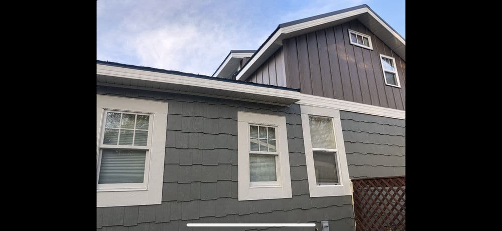 Modern two-story house with gray and brown siding, white trim, and multiple windows.