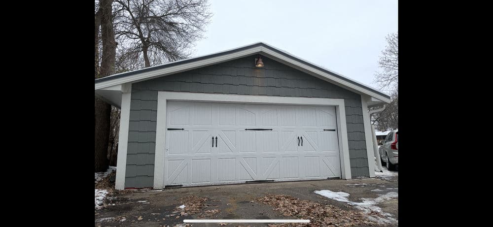 Gray garage with white double doors and exterior light, surrounded by a snowy landscape.