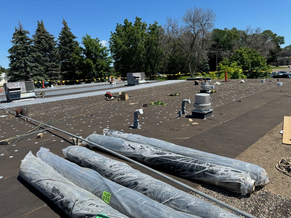 Roofing project with rolled materials and HVAC units under clear blue sky and trees.