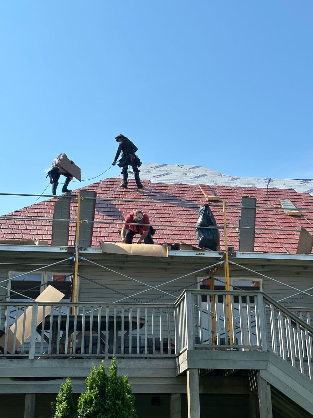 Roofing contractors installing new shingles on a residential home under a clear blue sky.