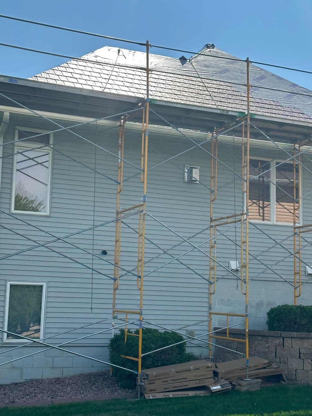 Scaffolding set up for roofing work on a residential house under clear blue skies.