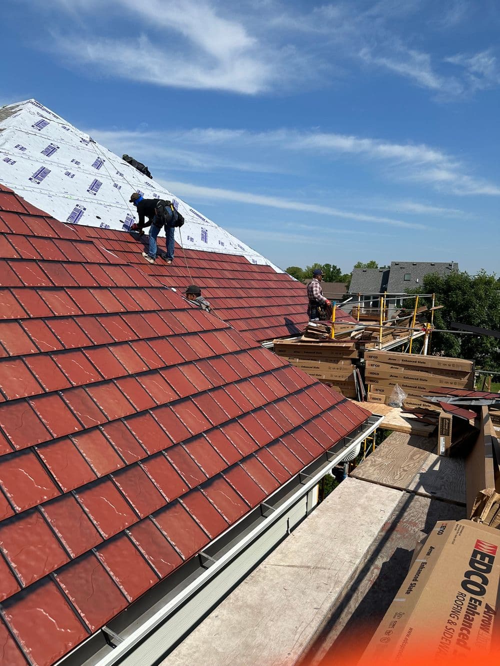 Workers installing new red tile roofing on a residential home under a clear blue sky.