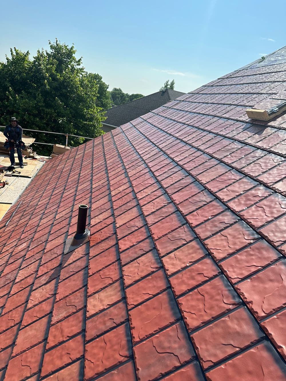 Red slate roof installation with workers and clear blue sky in the background.
