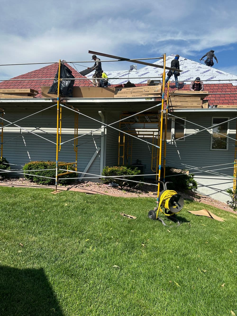 Roofing crew installing new shingles on a residential house with scaffolding and tools visible.