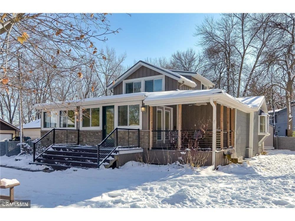 Modern home with a spacious front porch, surrounded by snow-covered trees. Ideal for winter living.