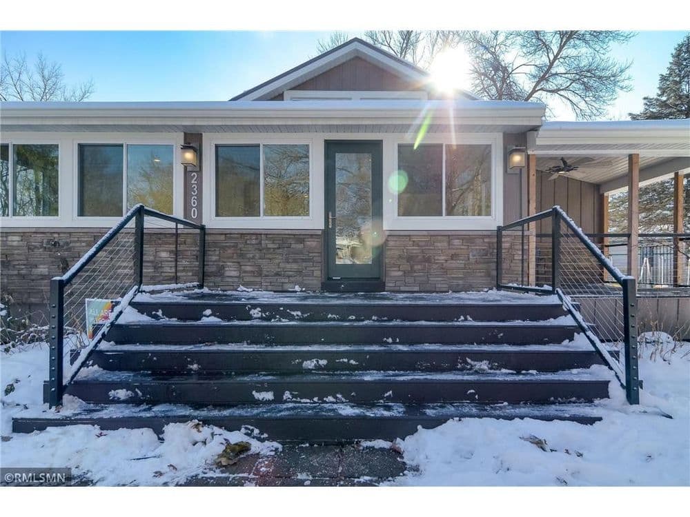 Front view of a home with large windows, snow-covered steps, and a sunlit entrance.