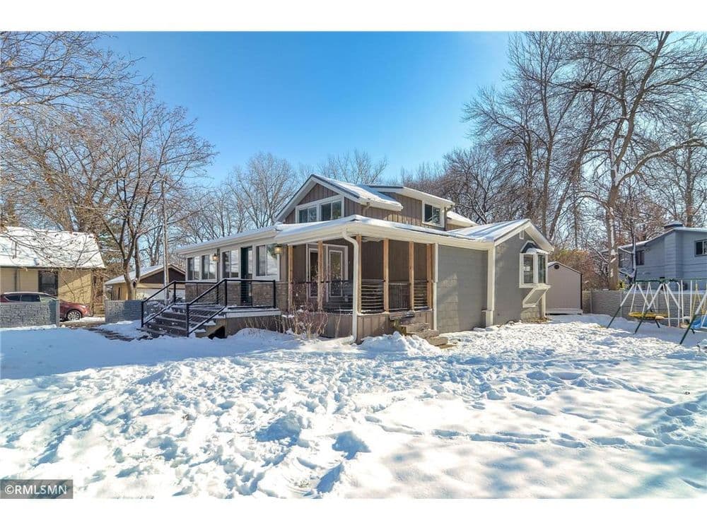 Cozy home with porch and snow-covered yard surrounded by trees in winter.