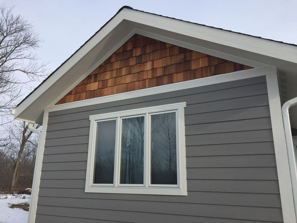 Modern house exterior featuring gray siding and cedar shake accents under a clear sky.