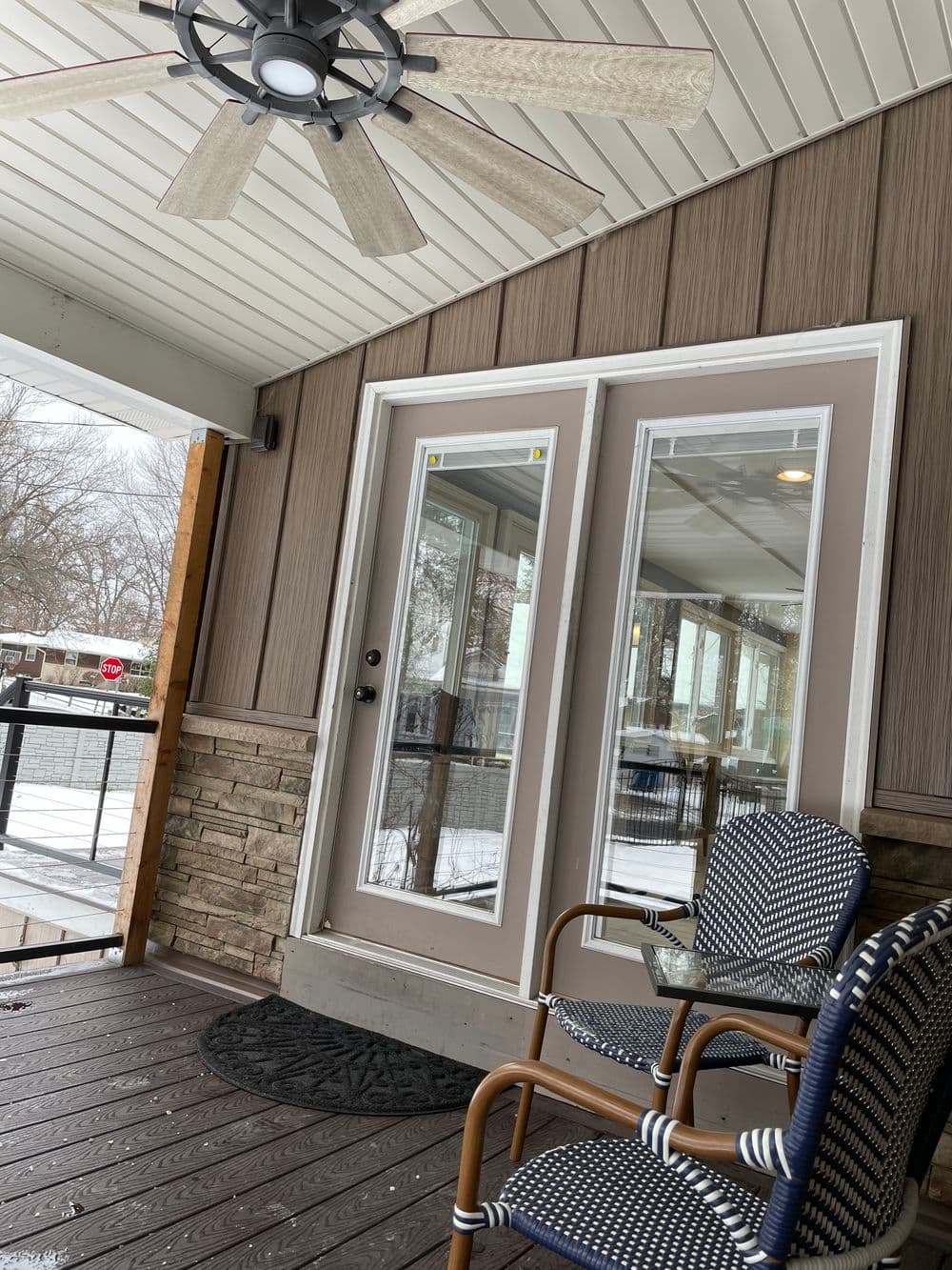 Modern porch featuring double glass doors, a ceiling fan, and stylish chairs.