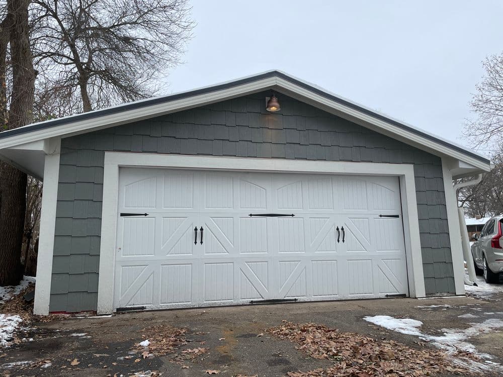 Gray garage with white double doors and decorative hardware, set against a wintry landscape.