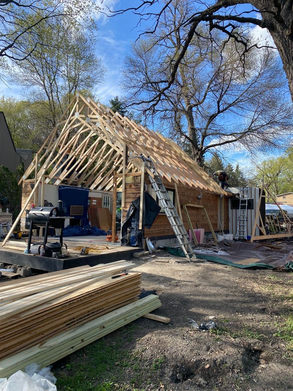 Construction site with wooden framing for a house renovation surrounded by trees and materials.