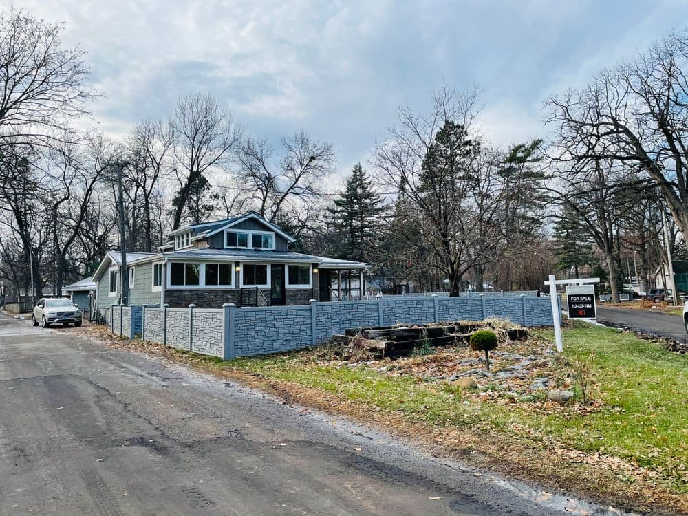 Charming house with stone fence on a quiet street, surrounded by trees and greenery.