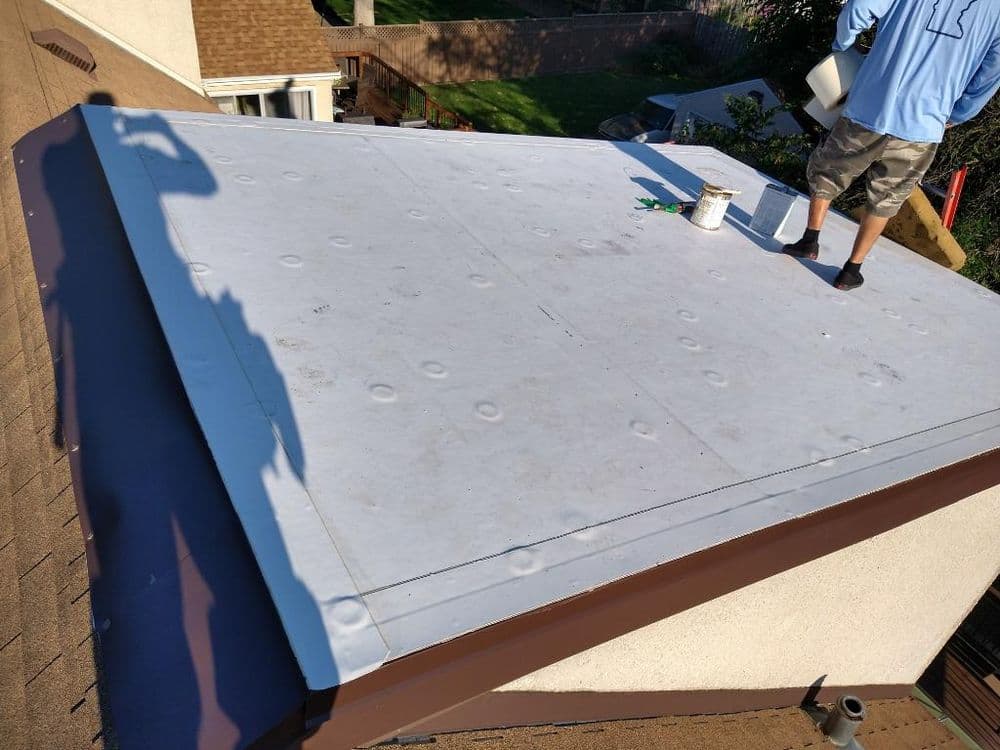 Rooftop installation with a worker applying material on a flat surface in daylight.