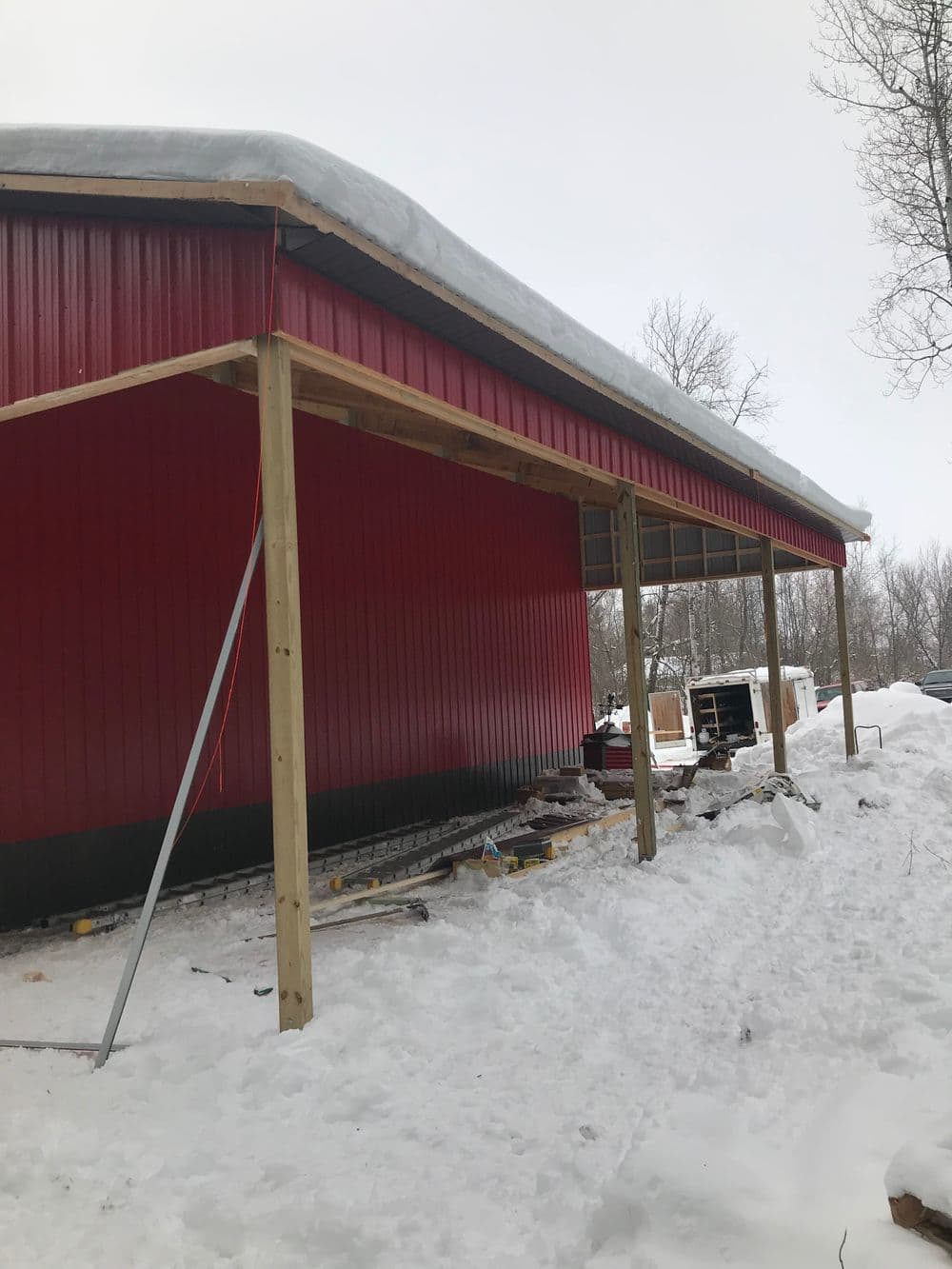Newly constructed red building with a sloped roof, partially surrounded by snow.