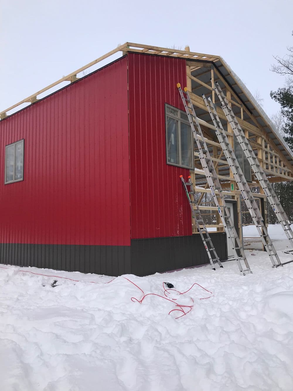 Red building under construction in snowy landscape with ladders and tools nearby.