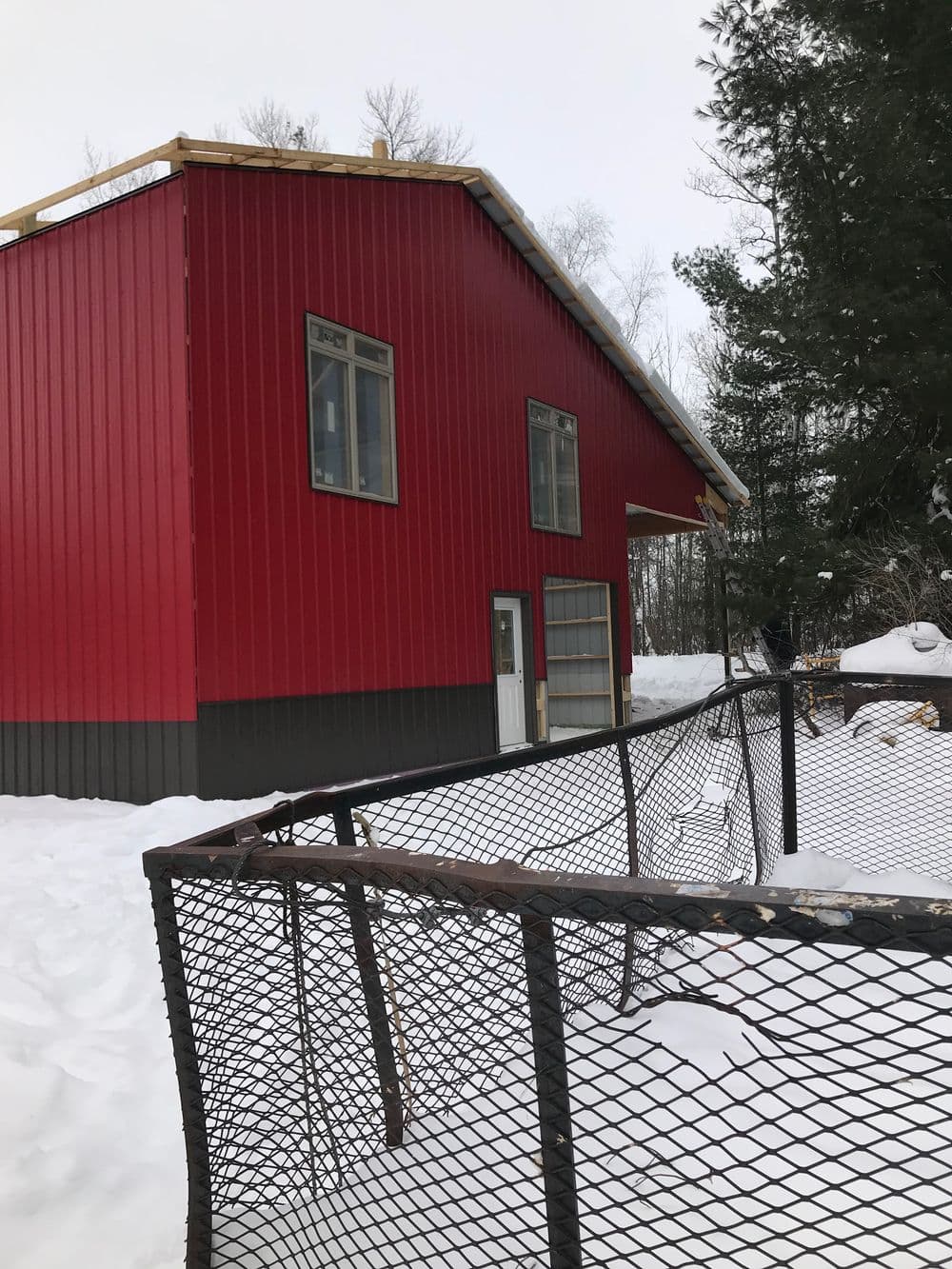 Red metal barn-style building in snowy landscape with a mesh fence nearby.