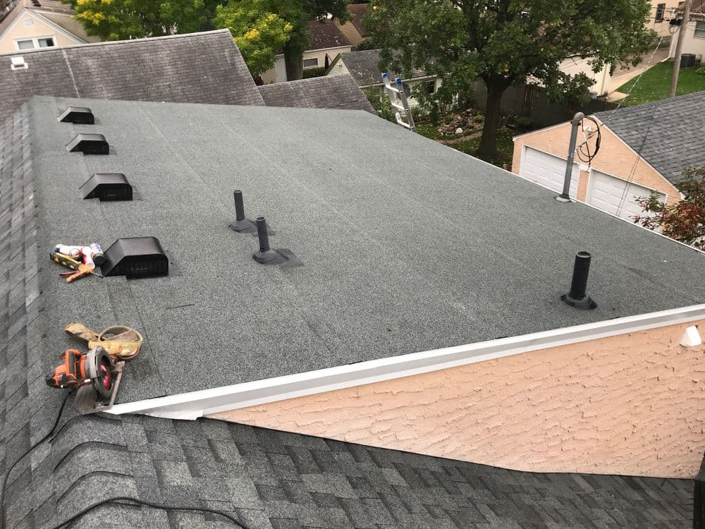 Newly installed gray asphalt roof with vents and tools on residential house.