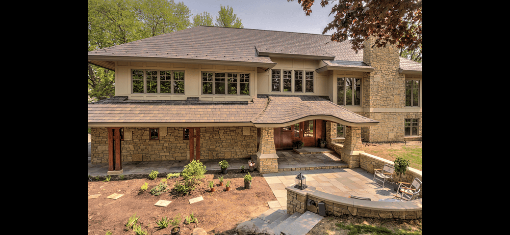 Modern stone house with large windows, lush garden, and elegant entryway in sunny setting.